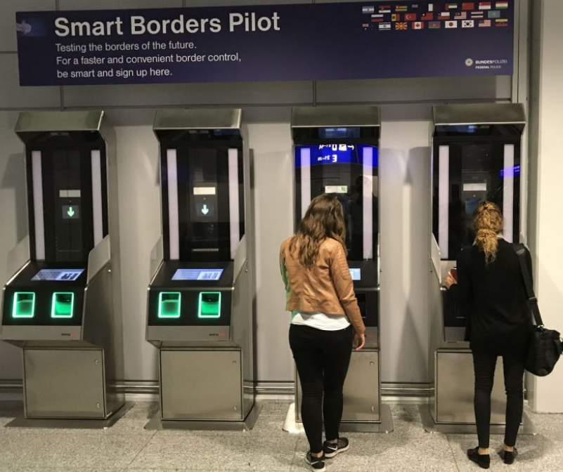 A modern airport self-service kiosk with a fingerprint scanner and camera, representing the new EU Entry/Exit System (EES) biometric border control for non-EU travelers.